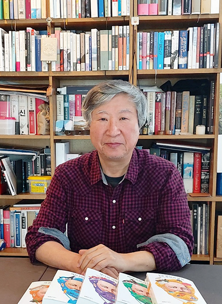 자주색 셔츠를 입은 김석희 번역가가 양손을 모으고 앉아있다. 그의 앞에는 『쥘 베른 걸작선』 5권이 가지런히 놓여있으며, 그의 뒤엔 책들이 빼곡하게 꽂혀있는 책장들로 꽉 차 있다.