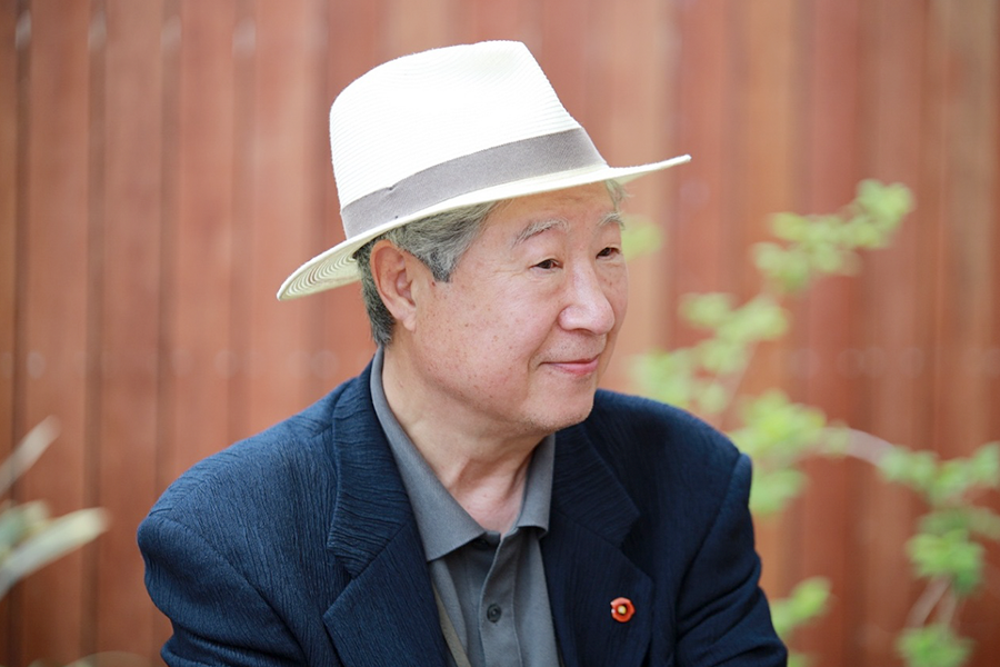 짙은 파란색 재킷과 회색 셔츠를 입고 하얀색 중절모를 쓴 김석희 번역가가 오른쪽을 바라보며 미소를 띠고 있다.