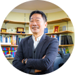 정장을 입은 김중섭 교수가 팔짱을 낀 상태로 비스듬히 서 정면을 보고 환하게 웃고 있다. 그의 뒤에는 컴퓨터 모니터와 빼곡하게 꽂혀있는 책장의 책들, 상패 등이 보인다.