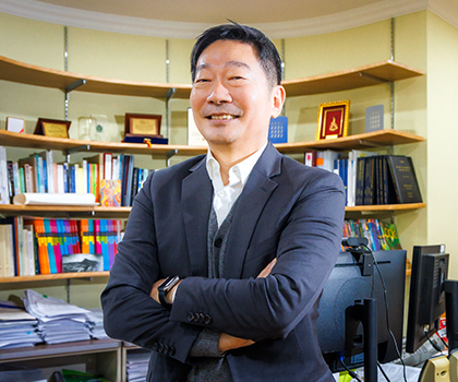 반갑습니다 기사 사진. 정장을 입은 김중섭 교수가 팔짱을 낀 상태로 비스듬히 서 정면을 보고 환하게 웃고 있다. 그의 뒤에는 컴퓨터 모니터와 빼곡하게 꽂혀있는 책장의 책들, 상패 등이 보인다.