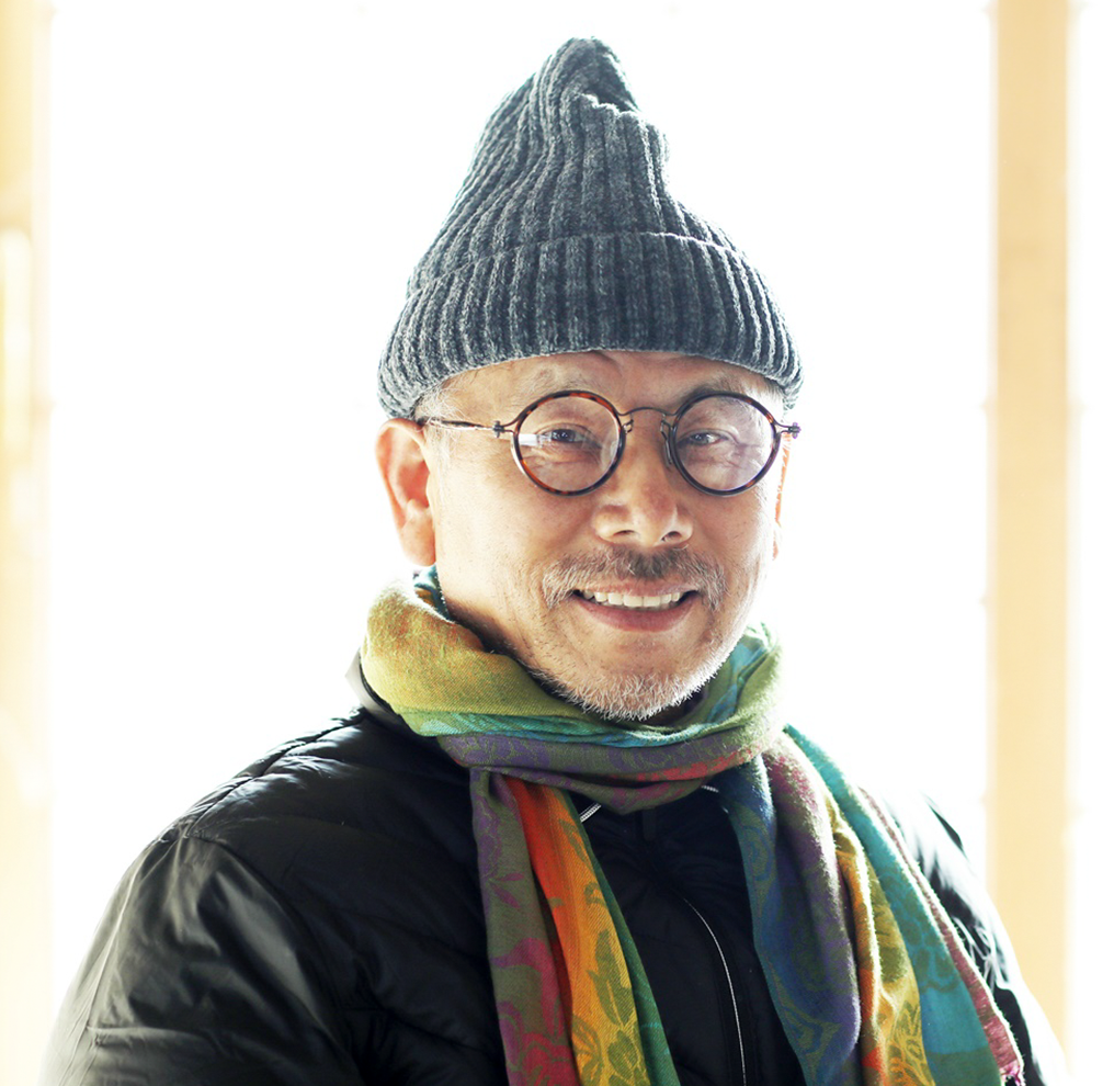 회색 모자를 쓰고 안경을 낀 김반석 작가가 비스듬히 서서 웃고 있다. 목에는 무지개색 목도리를 둘렀다.