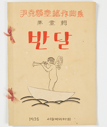 사진 상단에는 윤극영가요작곡집 제1집이라고 한자로 써있고, 그 밑엔 반달이라는 글씨가 쓰여 있다. 중앙에는 머리에 왕관과 날개를 단 소년이 작은 배를 타고 트럼펫을 불고 있는 그림이 있다. 그밑엔 1926 서울마리아회라고 쓰여 있다.