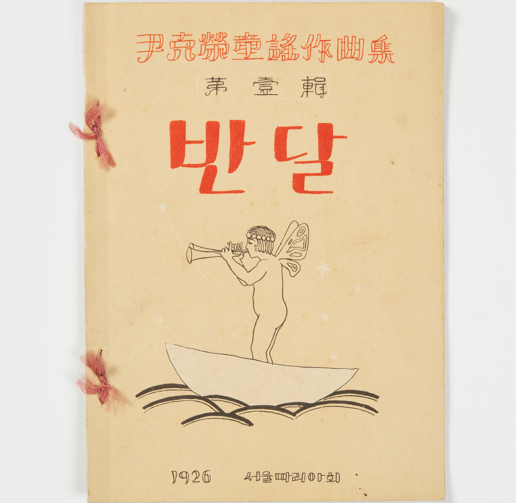 사진 상단에는 윤극영가요작곡집 제1집이라고 한자로 써있고, 그 밑엔 반달이라는 글씨가 쓰여 있다. 중앙에는 머리에 왕관과 날개를 단 소년이 작은 배를 타고 트럼펫을 불고 있는 그림이 있다. 그밑엔 1926 서울마리아회라고 쓰여 있다.