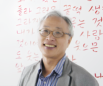 안경을 쓴 이기갑 목포대 교수가 웃고 있고, 그의 뒤에는 빨간색으로 쓰인 글자가 있다.