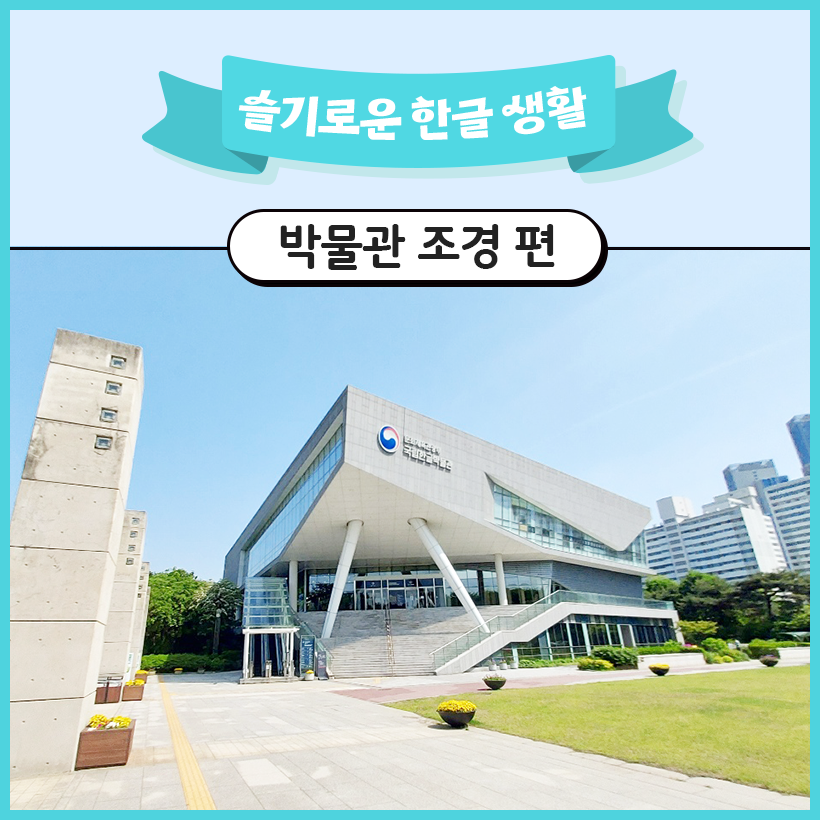 국립한글박물관의 전경이 펼쳐져 있다. 국립한글박물관 건물 앞에는 잔디밭과 꽃들이 있으며, 오른쪽에는 아파트들이 있다.