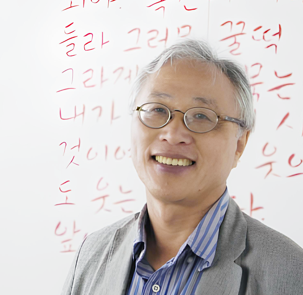 반갑습니다 사진. 안경을 쓴 이기갑 목포대 교수가 웃고 있고, 그의 뒤에는 빨간색으로 쓰인 글자가 있다.