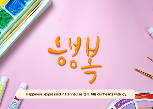 ‘내가 만난 한글 사진영상 공모전 전시’ 영상 부분 대상 수상자인 인도네시아 
NindyaRatnaUtari 씨의 ‘한글: 감정의 언어’ 영상 중 한 장면이다. 분홍색 배경 가운데 주황색 물감으로 짜놓은 ‘행복’이라는 글자가 적혀 있다. 글자 주위에는 물감과 팔레트가 놓여 있다.