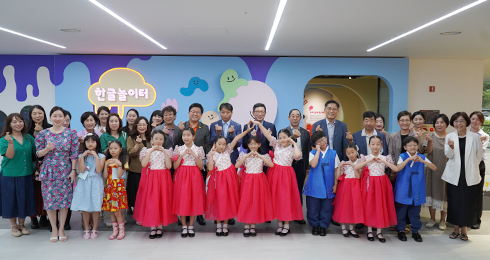 한글놀이터 순회전 ‘나의 특별한 하루’ 개막식 행사 현장 사진이다. ‘한글놀이터’가 적혀 있는 벽 앞에서 여러 명의 어린아이와 어른들이 함께 서 있다. 앞줄에 서 있는 어린이들은 전통 한복을 입고 있으며 손으로 하트를 만드는 자세를 취하고 있다. 뒷줄에 서 있는 성인들은 주로 정장을 입고 있으며 활짝 웃고 있다.
