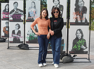 ‘한글 멋글씨 사진전’에 참가한 박시현, 박성민 작가 사진이다. 분홍색 옷을 입고서 한 쪽 손을 허리에 두고 웃고 있는 박시현 작가 옆에 그의 팔짱을 끼고 서 있는 박성민 작가가 있다.
