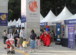 ‘2024 한글주간’ 현장 모습이다. 사진 중앙에는 부모님 손을 잡고 서 있는 아이들이 있다. 한 아이는 세종대왕 옷을 입은 사람과 마주 보고 있다. 뒤편으로는 체험 부스들이 나란히 줄지어있고, 박물관 기둥에는 ‘2024 한글주간’ 포스터가 붙어있다.