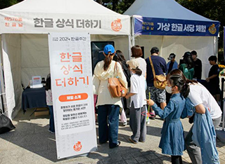‘2024 한글주간’ 현장 모습이다. ‘한글 상식 더하기’ 체험 부스 앞에서 사람들이 한글 상식 퀴즈를 풀기 위해 줄을 서 있다. 청원피스를 입은 아이가 ‘한글 상식 더하기’ 체험 소개가 적힌 팻말을 바라보며 손가락으로 가리키고 있다.