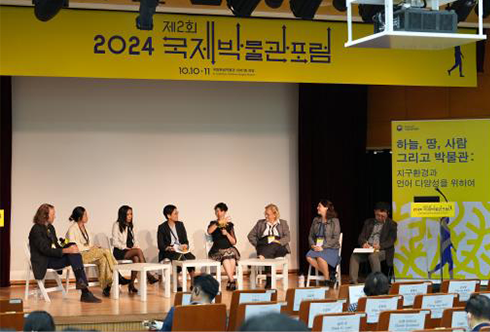 제2회 국제박물관포럼 사진이다. 중앙에 무대가 있고 무대 위에는 여러 명의 발표자가 앉아 발언자의 이야기에 귀 기울이며 경청하고 있다. 무대 위쪽에는 노란색 현수막이 걸려 있으며, ‘2024 제2회 국제 박물관 포럼’이라고 적혀 있다.