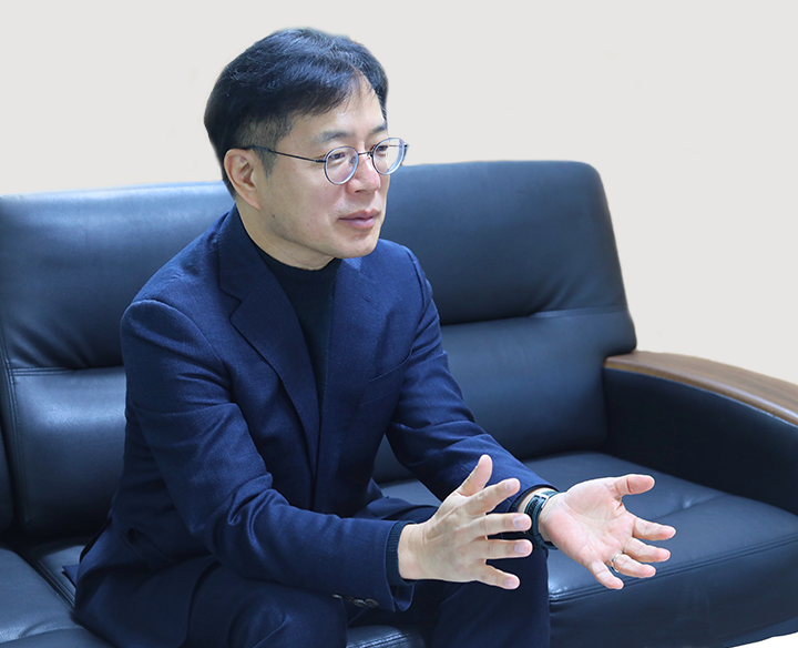 검은색 소파에 앉아 있는 강정원 관장이 앞을 바라보며 대화하고 있는 모습이다. 두 손을 앞으로 내밀며 적극적으로 대화에 참여하고 있다.