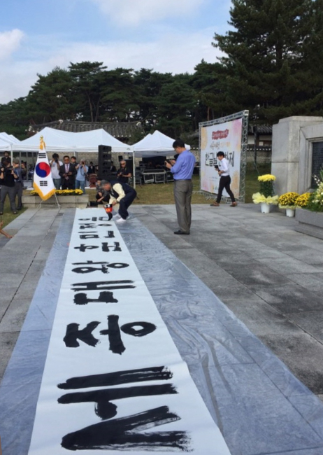 권명원 서예가가 여주 세종대왕릉 한글날 571돌 행사에서 한글 서예를 선보이고 있다. 긴 두루마리 앞에 서서 붓을 들고 ‘세종대왕 훈민정음’이라는 문구를 써 내려가고 있다.