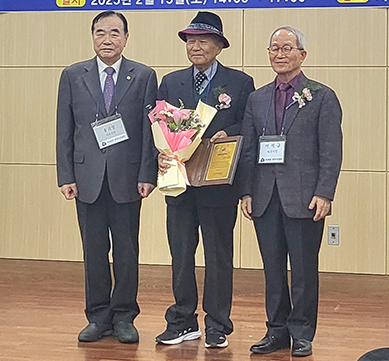 반갑습니다 사진. 양복을 입은 세 남성이 나란히 서 있다. 오른쪽 남성은 짙은 회색 양복을 입고 있고, 이름표를 목에 걸고 있다. 가운데 남성은 (사)한국시조협회 김달호 세계화위원장으로, 중절모를 쓰고 있다. 한 손에는 꽃다발, 다른 한 손에는 표창장을 들고 서 있다. 왼쪽 남성 역시 정장 차림이며, 그의 옷에는 핀으로 고정된 작은 꽃장식이 있다.