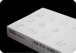 국립한글박물관 10주년 기념 백서 ‘한글 전시: 10개의 질문’ 사진이다. 책 표지는 흰색이고 다양한 한글 자모가 그려져 있다. 책등에는 ‘2014-2024 국립한글박물관 전시디자인 백서’가 적혀 있다.