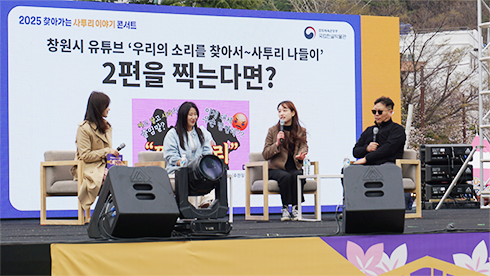 창원시청 뉴미디어팀의 사투리 영상 제작 뒷이야기를 들을 수 있었던 행사 사진이다. 무대 위에 창원시청 뉴미디어팀에서 나온 여성 직원 세 명이 의자에 앉아 있고, 그 옆에 선글라스를 착용한 남자 MC가 앉아서 그들의 이야기를 듣고 있다. 뒤쪽 스크린에는 ‘창원시 유튜브 우리의 소리를 찾아서-사투리 나들이 2편을 찍는다면?’이라는 글귀가 크게 적혀있다.