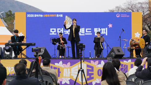 모던국악밴드 탈피가 사투리 공연을 하고 있다. 가운데에는 여성 보컬이 한손에 부채를 들고 노래를 부르고 있다. 뒤쪽에는 건반, 해금, 가야금, 장구를 연주하는 연주가가 있다.