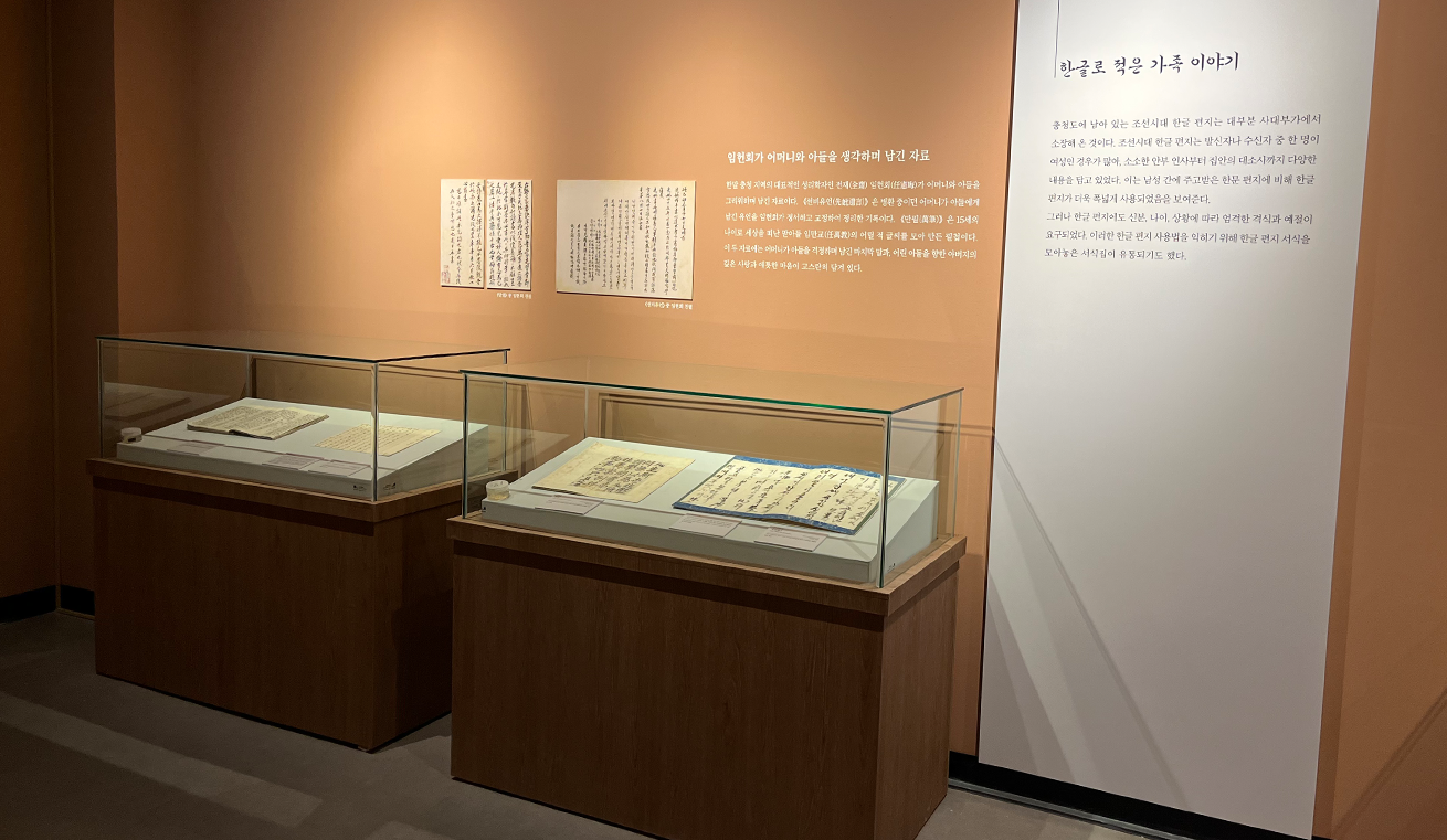 ‘한글 마음을 적다’ 전시 전경 사진이다. 두 개의 유리 진열장이 나란히 놓여 있으며, 안에는 붓글씨로 쓰인 옛 한글 문헌이 정갈하게 펼쳐져 전시되어 있다.
