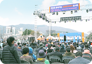 ‘2025 찾아가는 사투리 이야기 콘서트’ 행사 사진이다. 무대 위쪽에는 가로로 긴 현수막이 걸려 있으며, ‘2025 찾아가는 사투리 이야기 콘서트’라는 문구가 적혀있다. 무대에는 흰색 상의와 체크무늬 하의를 맞춰 입은 진해안젤루스 소년소녀 합창단원들이 일렬로 서 있다. 관객석에는 다양한 연령대의 사람들이 앉아 있다. 왼쪽 하단에는 하늘색 박스 안에 ‘기획기사’ 문구가 적혀있다. 하단에는 기사의 제목 ‘진해 군항제와 함께한 봄맞이 현장 찾아가는 사투리 이야기 콘서트’가 적혀있다.