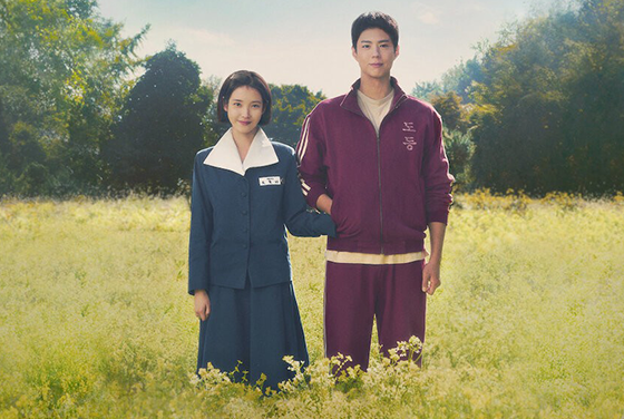 드라마 ‘폭싹 속았수다’ 스틸컷이다. 유채꽃밭에 서 있는 ‘애순’역의 아이유와 ‘관식’역의 박보검 배우가 나란히 서 있다. 옛날 여성 교복을 입고 있는 아이유는 자주색 체육복을 입고 있는 박보검의 주머니에 한쪽 손을 넣고 수줍게 웃고 있다.