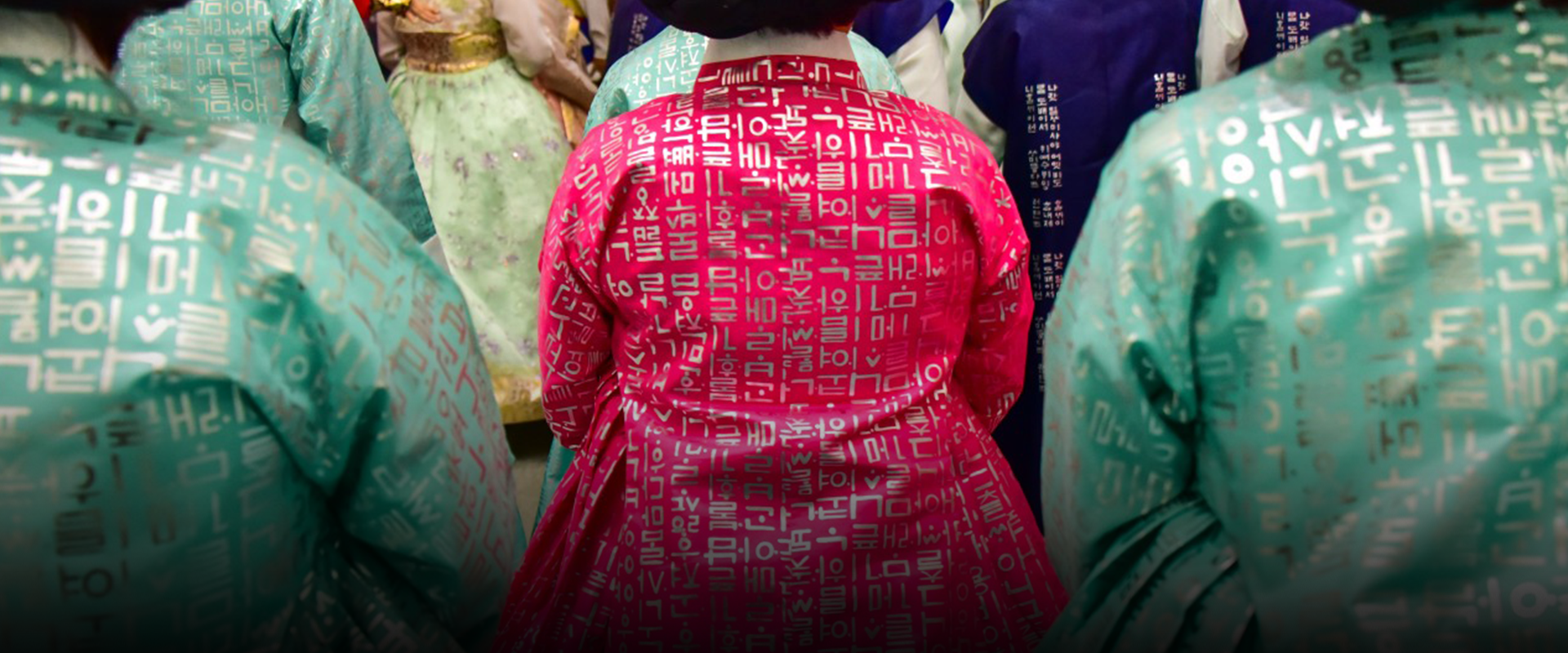 한글 자모와 단어가 새겨진 한복을 입은 여성들의 뒷모습이 찍힌 사진이다. 여성들은 조선시대 여성이 머리숱을 많아 보이게 하거나 머리 모양을 꾸미기 위해 머리에 얹었던 가체를 하고 있다. 가운데 여성은 진한 분홍색 저고리를 입었고, 그 주위 여성은 옥색 저고리를 입고 있다.