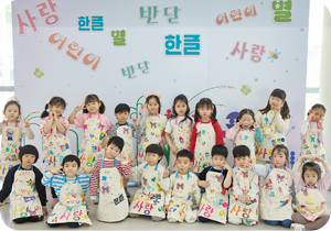 알록달록 한글 패션쇼’에 참여한 아이들 단체 사진이다. ‘사랑’, ‘어린이’, ‘한글’, ‘별’ 등이 적혀있는 흰 벽을 배경으로 여러 명의 아이가 모여 있다. 아이들은 모두 자신이 만든 앞치마를 입고 있으며, 손으로 하트를 만든다거나 머리에 손을 얹는 등 자유로운 포즈를 취하고 있다. 왼쪽 하단에는 하늘색 박스 안에 ‘기획기사’ 문구가 적혀있다. 그 아래에는 기사의 제목 ‘한글을 디자인적 관점으로 재해석하다! 근대한글연구소 & 알록달록 한글 패션쇼’가 적혀있다.