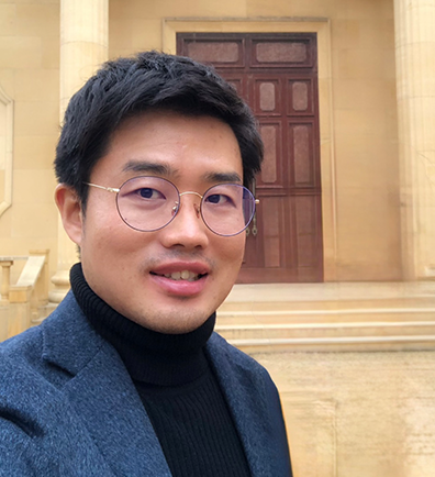 네이버 해피빈 이상태 기획자 사진이다. 자켓과 검은색 목폴라를 입고 있고 안경을 착용하고 있다. 신전으로 보이는 유물 앞에서 환하게 웃고 있다.