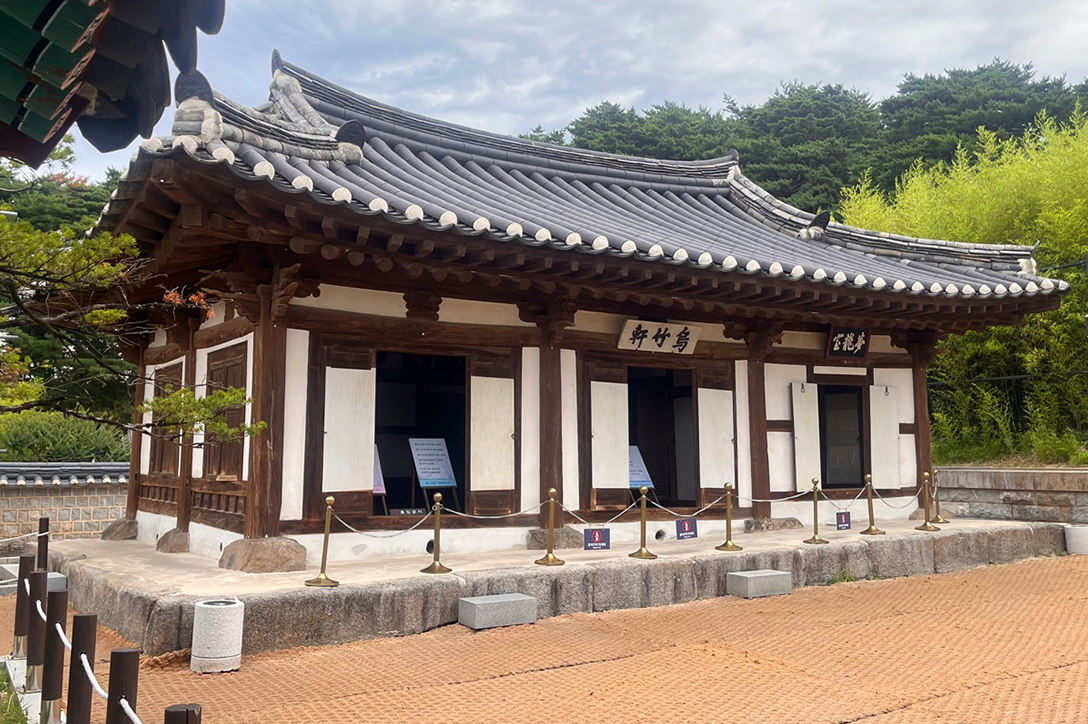 ‘오죽헌’ 외관 사진이다. 목조 기둥과 흰 벽면이 조화를 이루고 있는 한옥 건물 한 채가 중심에 있다. 그 주변을 울창한 나무들이 둘러싸고 있다.