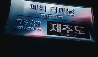 커다란 전광판처럼 생긴 구조물에 ‘페리 터미널(FERRY DEPOT)’이라고 크게 쓰여 있고, 그 아래에는 ‘다음 출발(NEXT DEPARTURE)’이라는 문구와 함께 도착지를 표시하는 전광판이 있다. 전광판에는 ‘제주도(Jeju Island)’라는 글자가 큼직하게 표시되어 있다. 한글 아래에 영어가 함께 표기되어 있다.