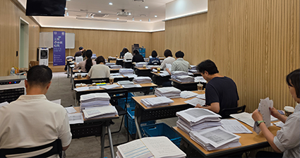 교보손글씨대회 예선심사 중인 심사위원들 사진이다. 심사위원들이 책상에 앉아 수많은 원고 더미를 하나씩 살펴보며 평가하고 있다.
