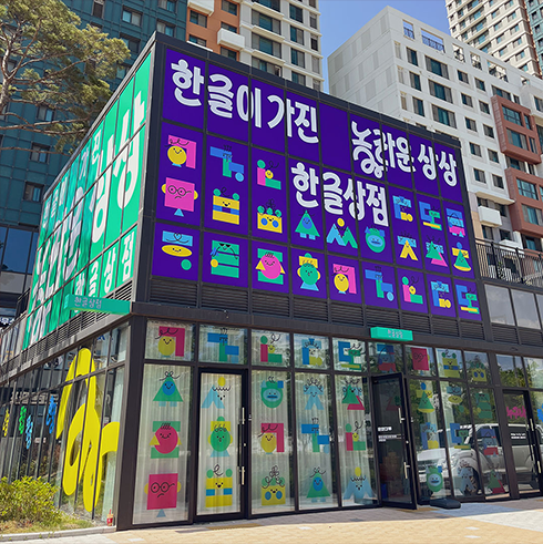 한글상점 건물 사진이다. 현대적인 건물 외관에 대형 현수막이 붙어 있는 모습이다. 현수막에는 ‘한글이 가진 놀라운 상상 한글상점’이라는 문구가 크게 적혀있으며, 화려한 색감의 장식이 외벽을 가득 채우고 있다. 