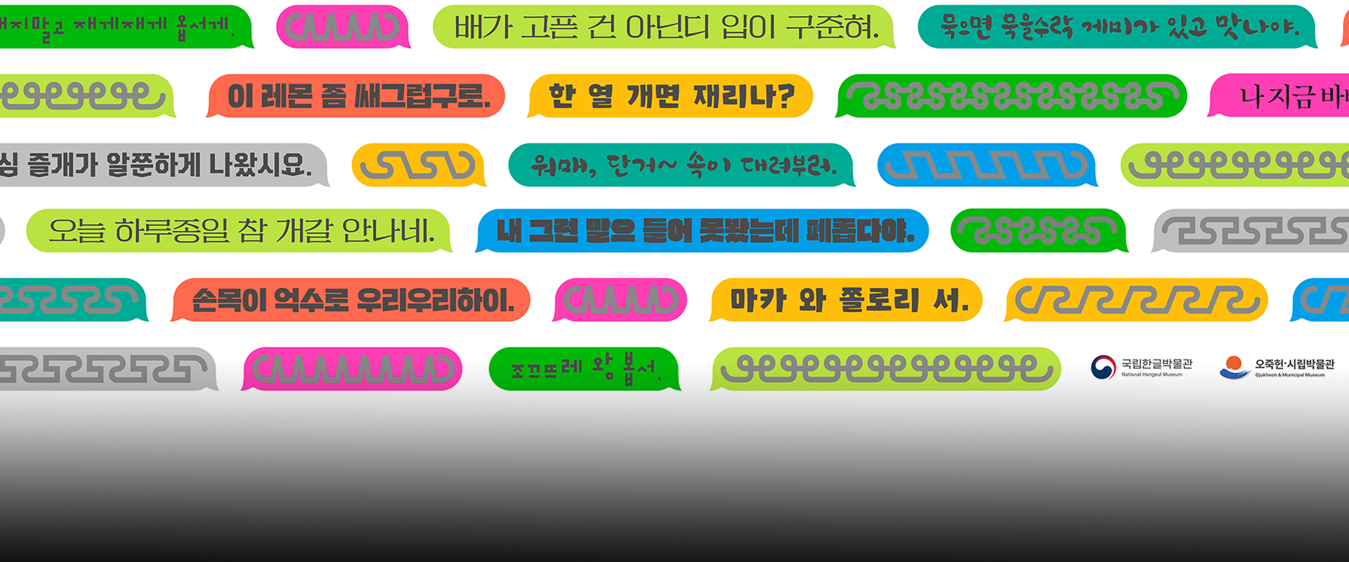 슬기로운 한글 생활 사진. 다양한 색상의 말풍선들이 화면 전체에 흩어져 있고, 각각의 말풍선 안에는 강릉 사투리가 적혀있다. 말풍선들은 연두, 주황, 분홍, 파랑, 회색, 초록 등의 색으로 구성되어 있으며, 손글씨 느낌의 글씨로 ‘한 열 개면 재리나?’, ‘배가 고픈 건 아닌디 입이 구준혀.’와 같은 문장이 쓰여 있다. 배경은 회색에서 검정으로 자연스럽게 그라데이션 처리되어 있다. 오른쪽 하단에는 국립한글박물관과 오죽헌·시립박물관의 로고가 나란히 배치되어 있다. 사진 하단에는 주황색 박스 안에 ‘슬기로운 한글생활’ 문구가 적혀있다. 그 아래에는 기사의 제목 ‘강릉 사투리의 세계 속으로, 어서 오시우야! 강릉에서 만나볼 수 있는 ‘사투리는 못 참지!’’가 쓰여있다.