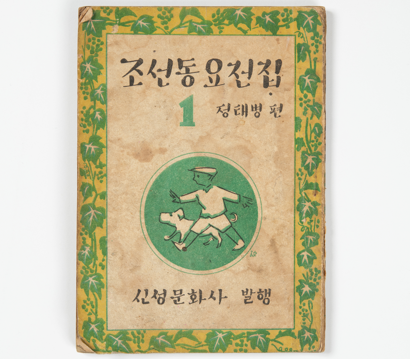 조선동요전집 1권의 표지 사진이다. 가장자리는 녹색 덩굴무늬로 장식되어 있고, 중앙 원 안에는 모자를 쓴 아이가 강아지와 함께 달리는 그림이 있다. 