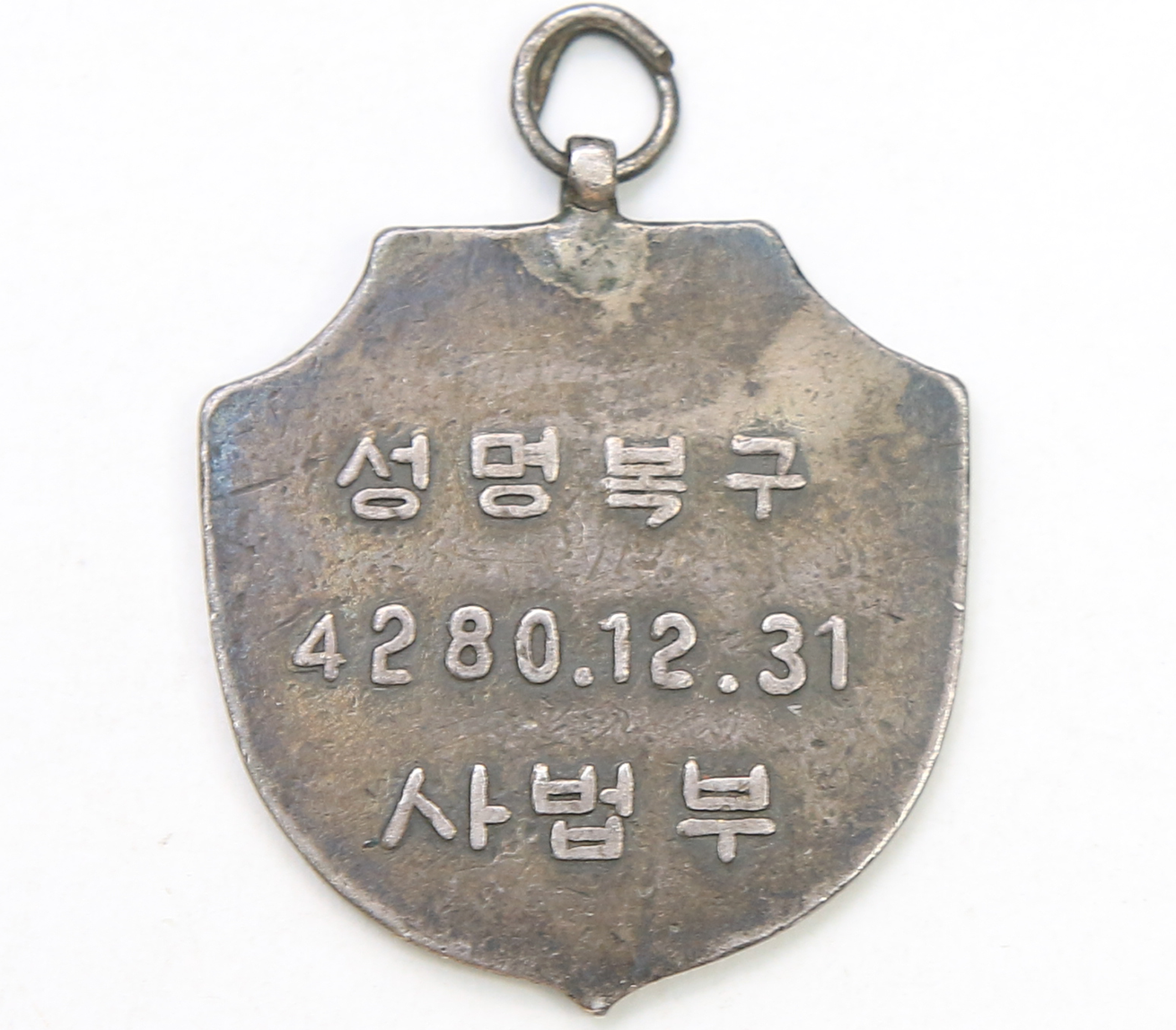 ‘성명 복구 기념 메달’ 사진이다. 왼쪽은 메달의 앞면으로, 전체가 은빛 금속이며 위쪽에는 고리를 달 수 있는 작은 고리가 붙어 있다. 중앙에는 ‘記念(기념)’와 ‘法(법)’이라는 글자가 크게 새겨져 있고, 양옆으로는 월계수와 꽃 모양 장식이 대칭으로 둘러싸고 있다. 오른쪽은 메달의 뒷면으로, 같은 방패 모양 안에 ‘성명복구’ ‘4280.12.31’ ‘사법부’라는 글자가 가로로 새겨져 있다.