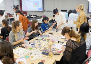 ‘한글 디자인 공방’ 수업을 참여하고 있는 외국인들의 모습이 담긴 사진이다. 여러 개의 긴 책상에 사람들이 옹기종기 모여 앉아 한글 디자인 공예작품을 만들고 있다.