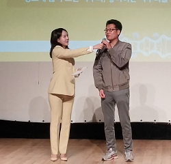 참여 관람객 사진이다. 노란 정장을 입은 사회자가 남성에게 마이크를 건네며 질문하고 있다.