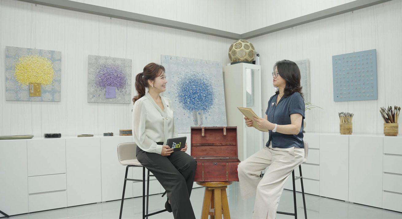 ‘궁금한글’ 김정민 작가 영상 속 한 장면을 캡처한 사진이다. 사회자와 김정민 작가가 마주보고 앉아서 이야기를 나누고 있다. 뒤에는 김정민 작가의 작품이 걸려있다.