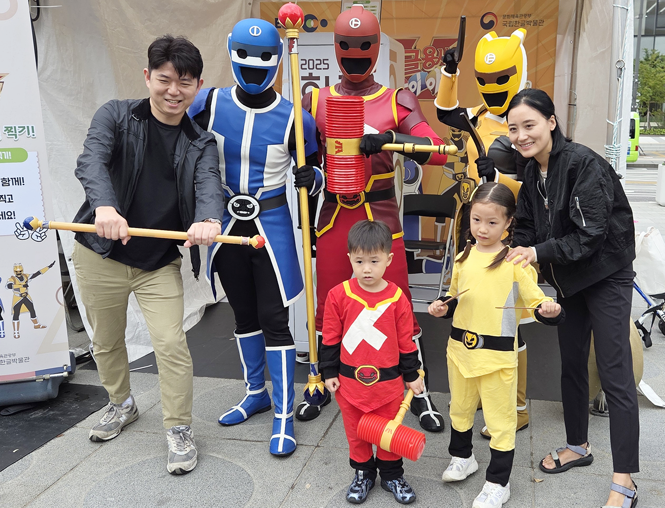 ‘2025 한글 한마당’ 국립한글박물관 체험 행사 현장 사진이다. 파란색, 빨간색, 노란색 슈트를 입은 ‘한글용사 아이야’와 아이들이 함께 기념사진을 찍고 있다.
