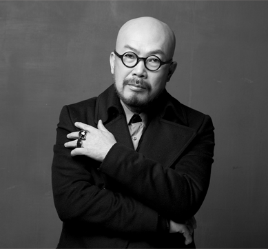 반갑습니다 사진. 이상봉 패션 디자이너의 모습이 담긴 흑백 사진이다. 이상봉 디자이너가 팔짱을 낀 채 카메라를 정면으로 응시하고 있다. 