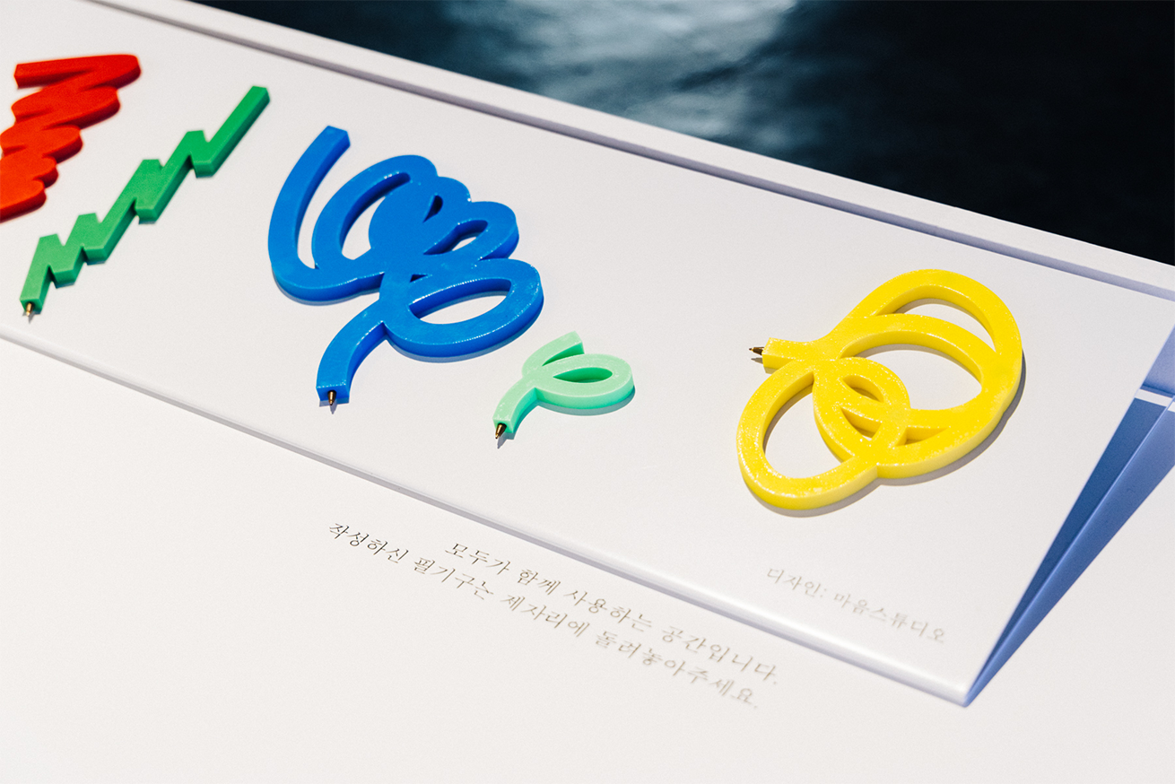 여러 색깔의 독특한 필기구가 하얀 전시대 위에 정렬되어 놓여있다. 곡선과 원형 등 추상적인 형태로 디자인되어 있다.