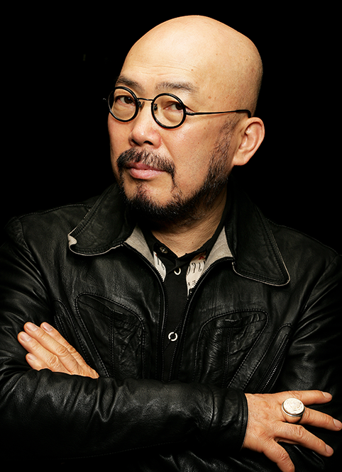 안경을 쓰고 검정 가죽 재킷을 입은 이상봉 디자이너가 비스듬히 고개를 돌린 채 카메라를 응시하고 있다.