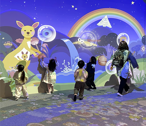 박물관은 지금 사진. 국립한글박물관 어린이 놀이터에 있는 인터랙티브 공간 ‘꿈꾸는 나의 방’에서 아이들이 스크린을 터치하며 체험하고 있다. 스크린에는 ‘ㄹ’, ‘ㅇ’, ‘ㅌ’ 같은 글자와 그와 연관된 알록달록한 그림들이 있다.