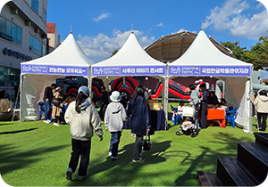 순천에서 열린 ‘찾아가는 사투리 이야기 콘서트’ 현장 사진이다. 흰색 천막 세 개가 나란히 서 있고, 각 천막의 현수막에는 흰 글씨로 각각 ‘언능언능 오이씨요~’, ‘사투리 이야기 콘서트’, ‘국립한글박물관이지라’라고 적혀있다. 천막 주변에는 체험하러 온 관광객들이 모여 있다.