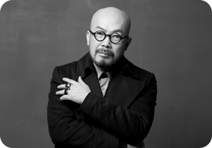 이상봉 패션 디자이너의 모습이 담긴 흑백 사진이다. 이상봉 디자이너가 팔짱을 낀 채 카메라를 정면으로 응시하고 있다. 