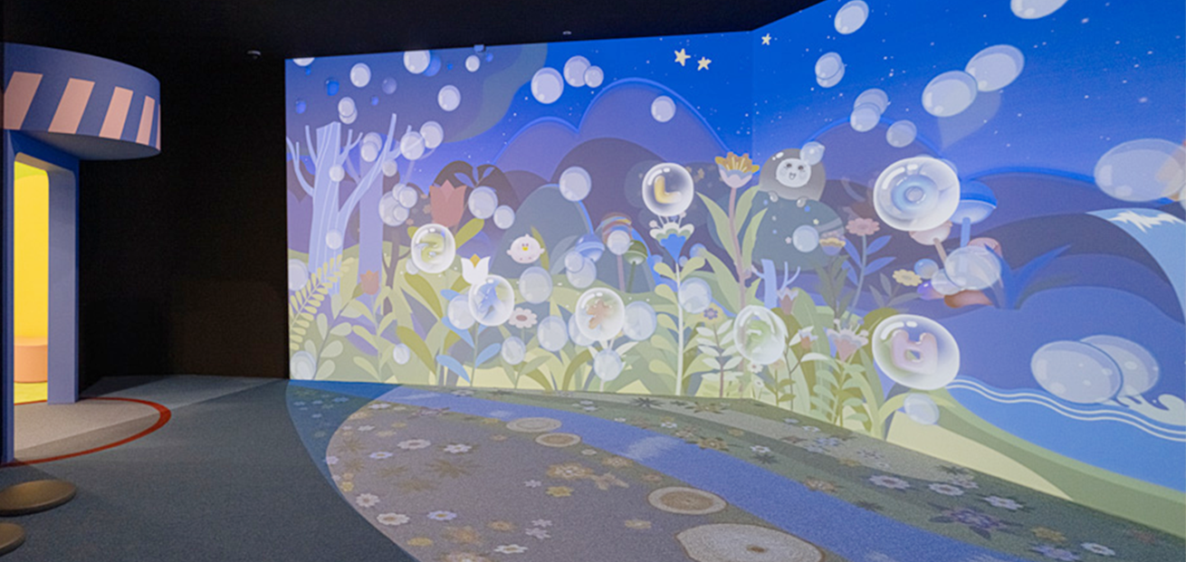 3부 ‘꿈꾸는 나의 방’ 내부 공간 사진이다. 대형 스크린 가득 밤하늘 아래 신비로운 숲의 풍경이 그려져 있으며, 그 위로 한글 자음이 담긴 투명한 비누 방울들이 떠다니고 있다. 숲속 곳곳에는 말랑통통 캐릭터가 숨어 있다.