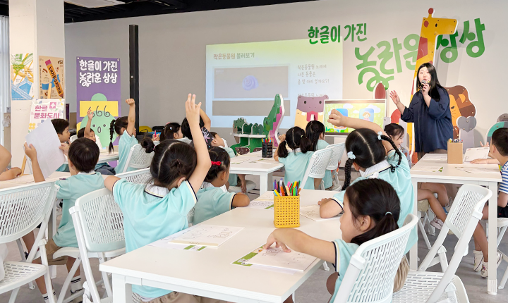 아이들이 책상에 둘러앉아 발표를 하기 위해 손을 들고 있다. 