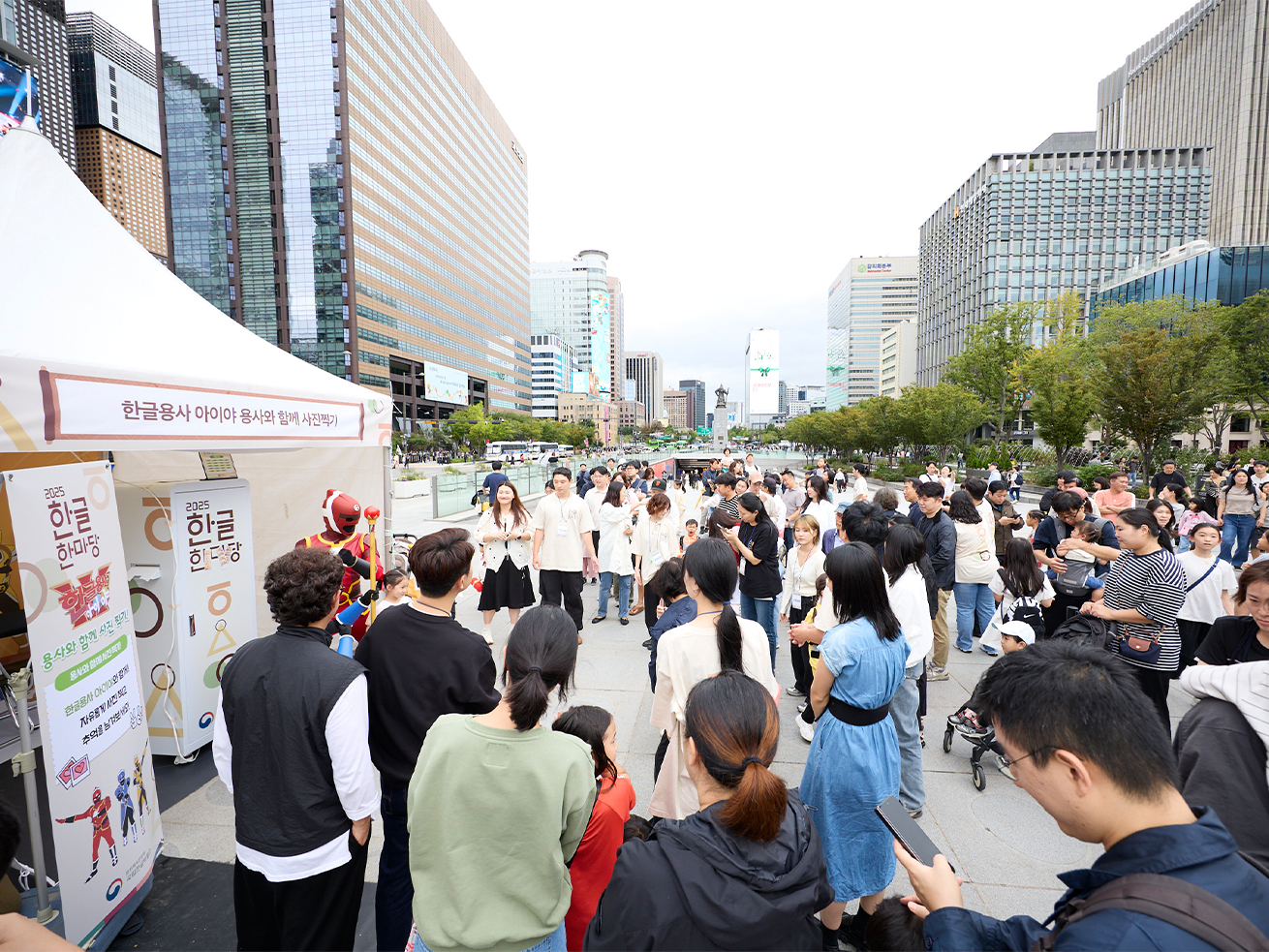 2025 한글한마당 행사 사진이다. ’한글용사 아이야 용사와 함께 사진찍기‘ 부스 앞에 여러 명의 사람이 모여 있다. 