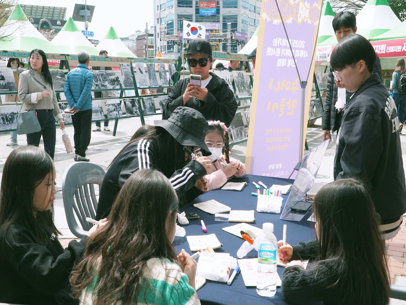 2025 사투리 체험 행사 사진이다. 아이들이 큰 테이블에 모여앉아 펜을 들고 무언갈 적고 있다.