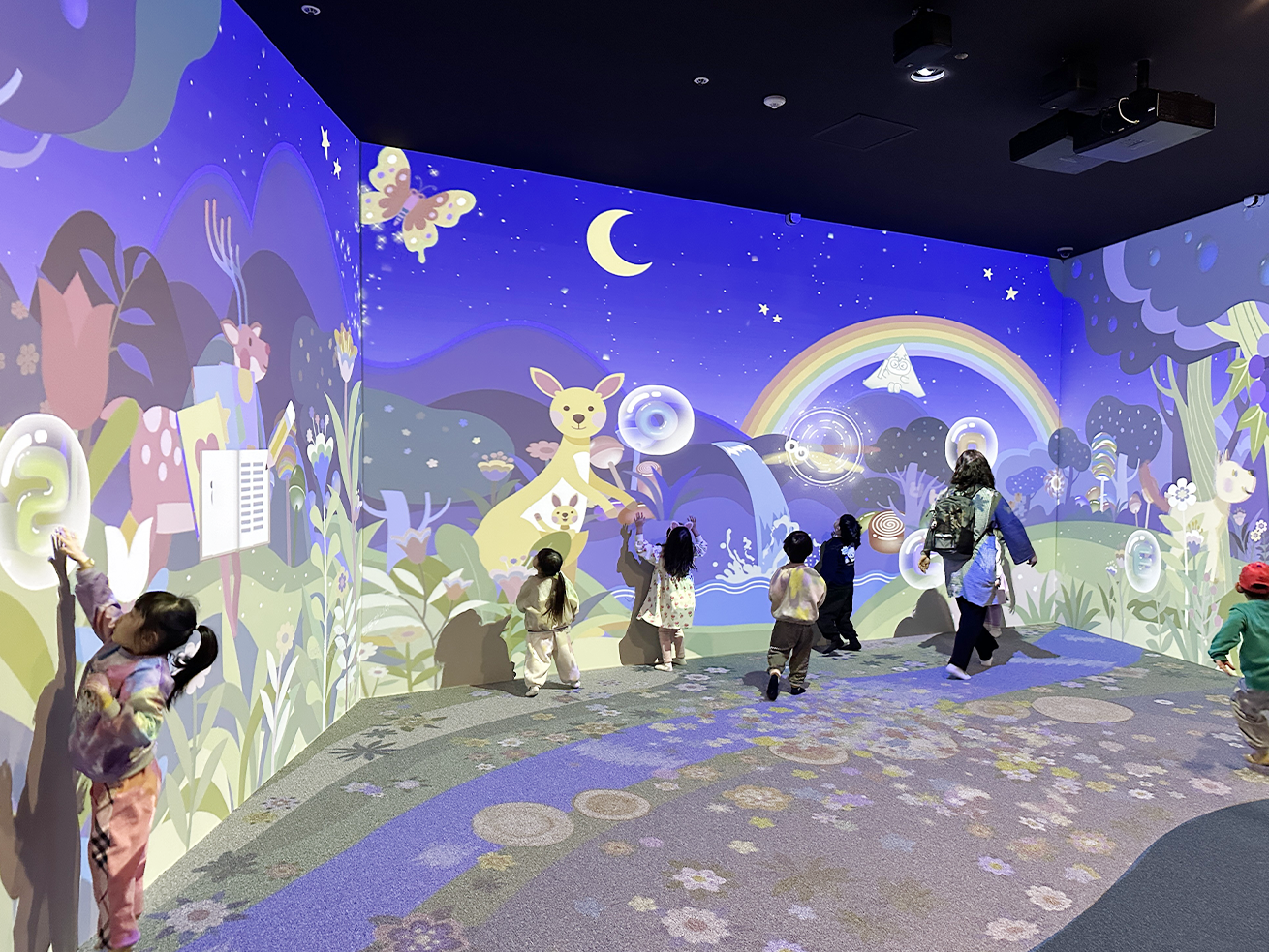 한글 놀이터 세종관 사진이다. 국립한글박물관 어린이 놀이터에 있는 인터랙티브 공간 ‘꿈꾸는 나의 방’에서 아이들이 스크린을 터치하며 체험하고 있다. 스크린에는 ‘ㄹ’, ‘ㅇ’, ‘ㅌ’ 같은 글자와 그와 연관된 알록달록한 그림들이 있다.